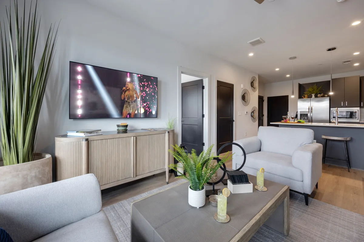 A lively and contemporary living space showcasing a sofa arrangement, green plants, a decorative cabinet, and a television displaying a performance scene, inviting guests for entertainment and relaxation.