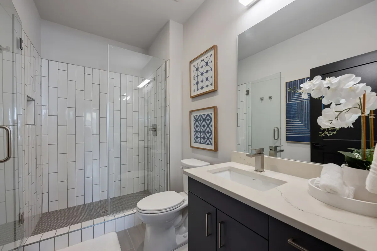 A modern bathroom featuring a glass shower enclosure, a sleek vanity with a sink, framed artwork, and a white orchid centerpiece. The space feels tranquil and refreshing, designed for relaxation and self-care routines.