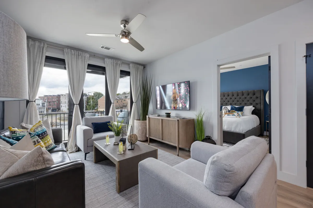 A comfortable and modern living room with a cozy seating area, large windows that offer a view and flood the space with natural light, a television for entertainment, and decorative plants adding a touch of freshness.