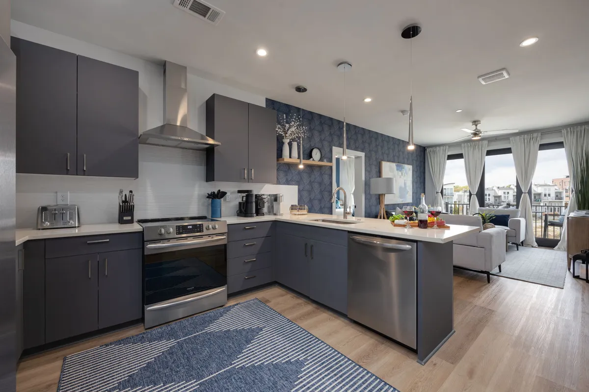A modern kitchen island anchors the space, surrounded by stainless steel appliances and decorative elements. Ample window views provide natural light, while the open layout encourages socializing and group activities like entertaining or family gatherings.