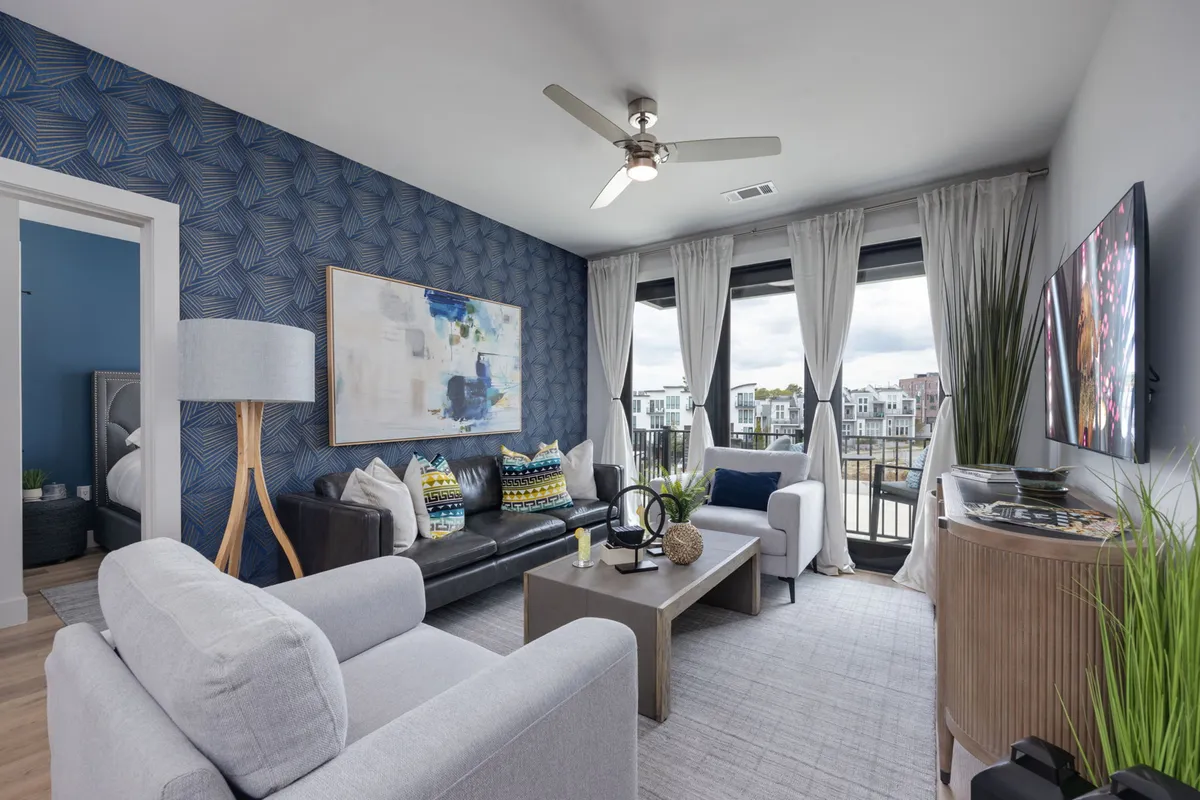 The image showcases a stylish living area with a textured blue accent wall, cozy seating, vibrant decorative artwork, and expansive windows that flood the space with natural light and reveal a glimpse of the vibrant Nashville skyline.